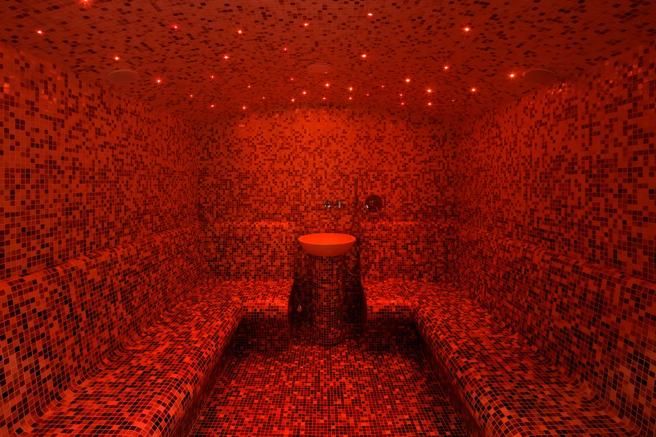 Il calidarium a mosaico illuminato di rosso, con il cielo stellato sul soffitto