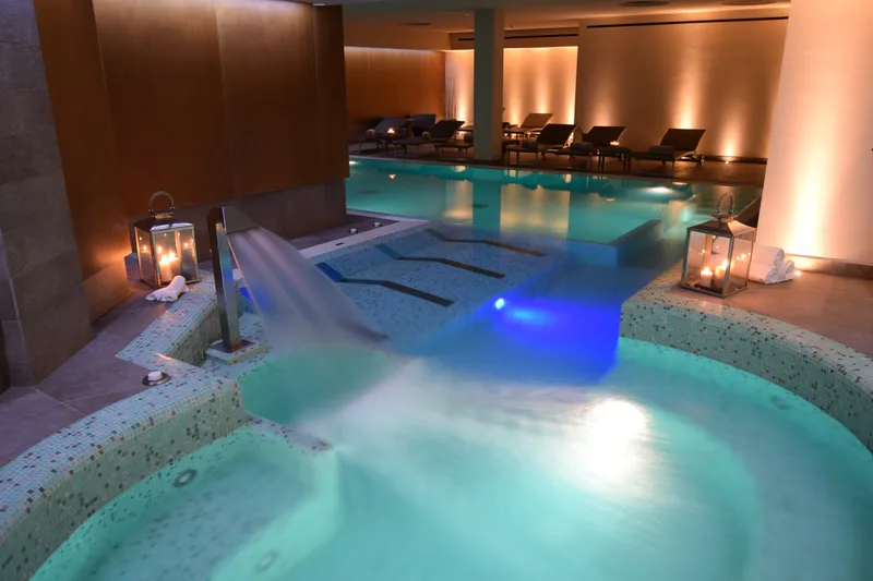 Piscina con idromassaggio e getti d'acqua. La vasca idromassaggio con la cascata d'acqua e le lanterne accese, e la piscina riscaldata sullo sfondo