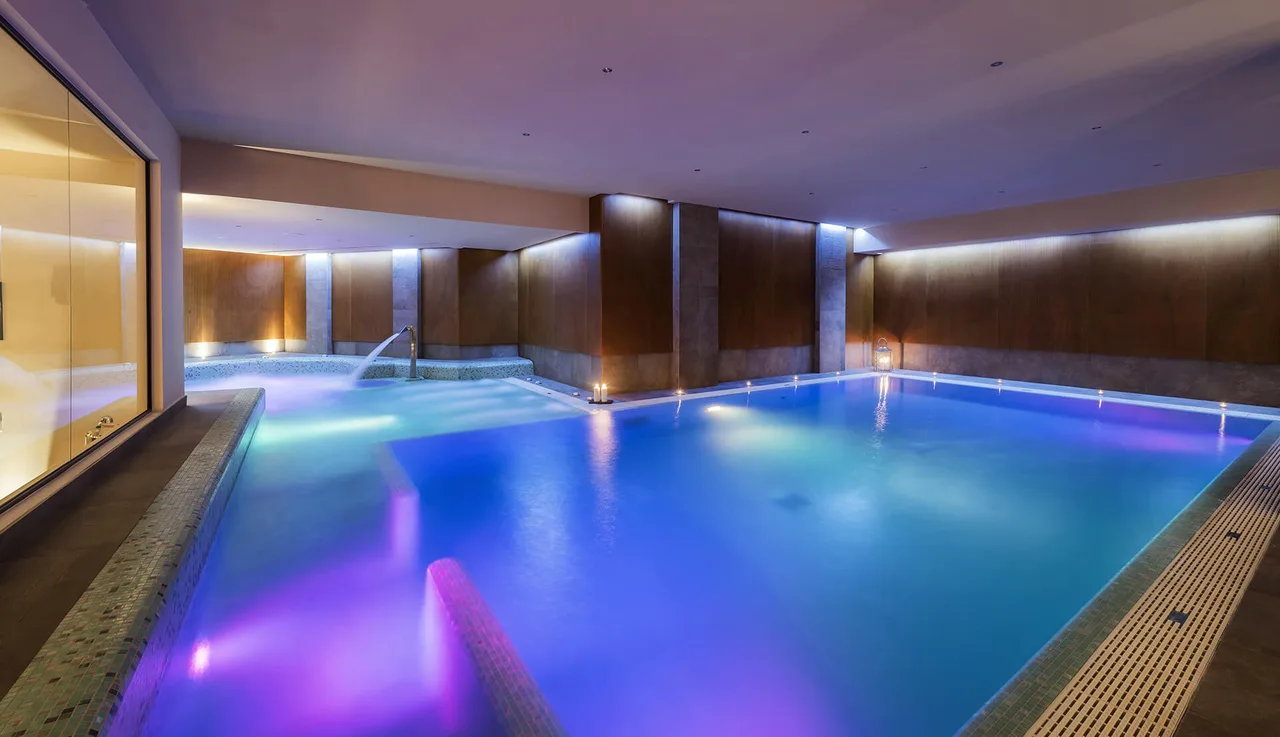 La piscina della Devero SPA illuminata di blu e viola, con le candele lungo il bordo