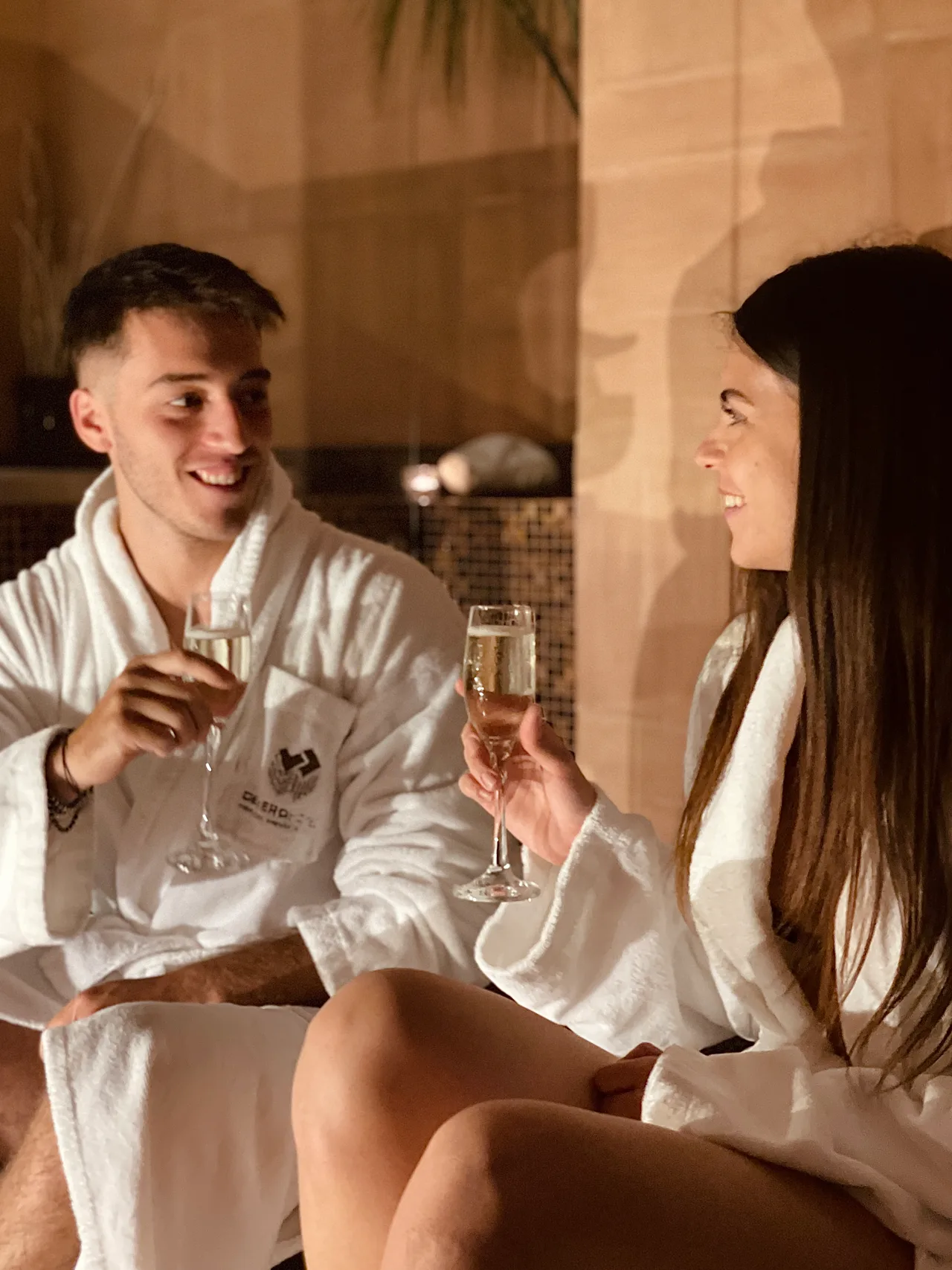 Due ospiti in accappatoio brindisano con un calice nella zona relax della Devero SPA.